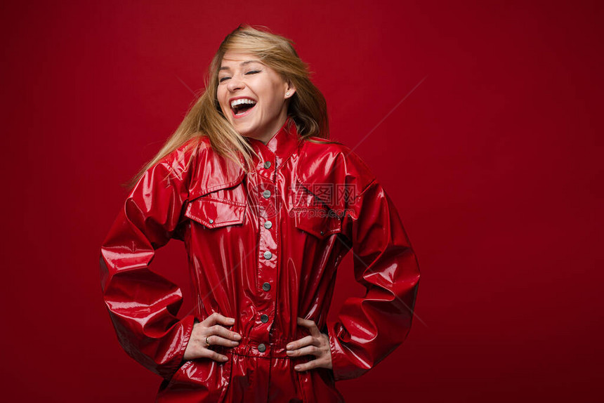 一个穿着时髦红色皮夹克的笑漂亮女孩的股票照片她被孤立在红色背景上笑着的金发女图片