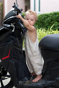 一个小男孩站在一辆摩托车的轮子后图片