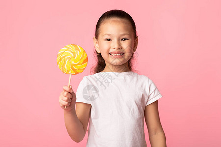 可爱的亚裔女孩笑着拿多彩棒糖被粉红色图片