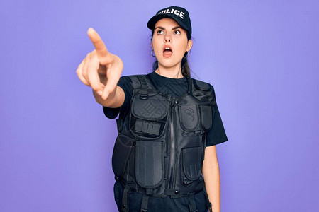 身穿紫色背景安全防弹背心制服的年轻女警用手指着前方惊讶图片