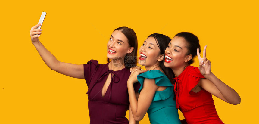 3个千禧年女孩使用电话照片拍摄自己在黄色背景中玩乐的照片图片