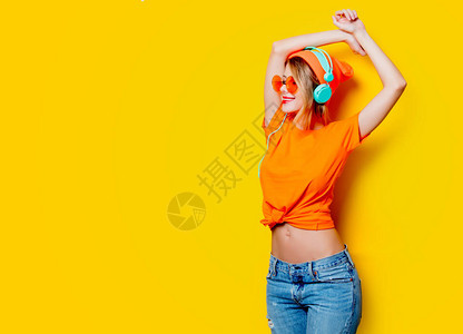 有橙色眼镜和黄色背景耳机的年轻时尚女青年图片