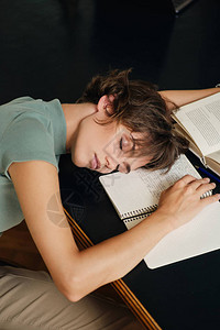 在大学图书馆学习时用书本和摘要坐在书桌上睡觉的年轻疲累女图片