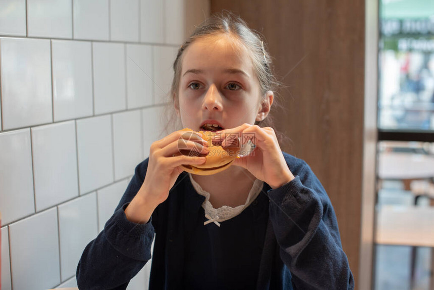 快乐的少女吃汉堡和炸薯条吃汉堡的女学生一个9岁的女孩在上学后带着汉堡吃午饭孩子喜欢吃午饭穿着图片