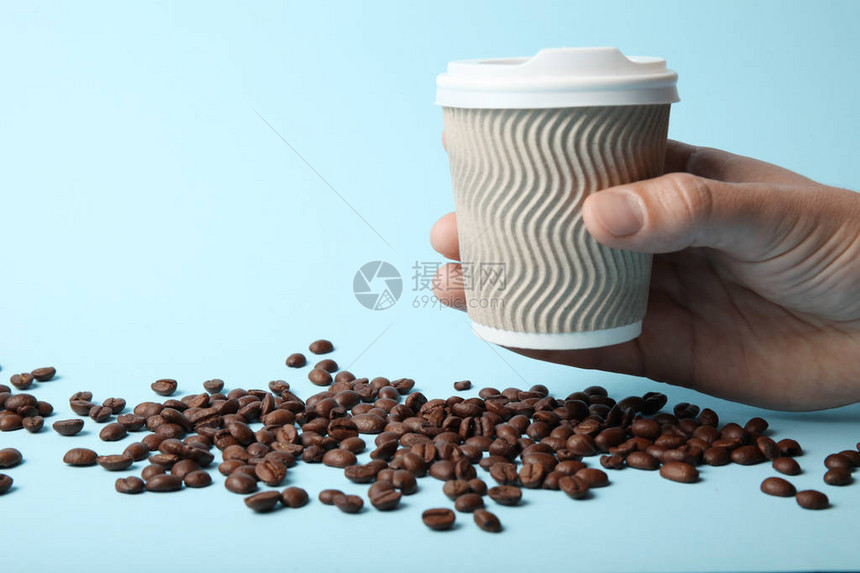 散落的咖啡豆和被手拿住的咖啡杯图片