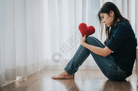 坐在床边的悲伤寂寞和忧郁的女人抱着红心在图片