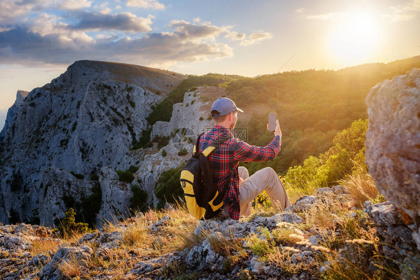强壮的男子徒步旅行者在山峰用智能手机拍照奇妙的黎明活动的概念和移动图片