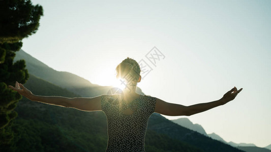 看着一位年轻女子站立迎接太阳从山上升起图片