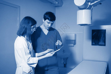 女和男放射科医生正在检查在医务室病人附近的药图片