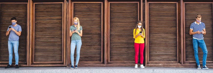 年轻人戴面罩使用手机保持社交距离图片