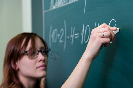在黑板教室上课的女教师解决了算术范例图片