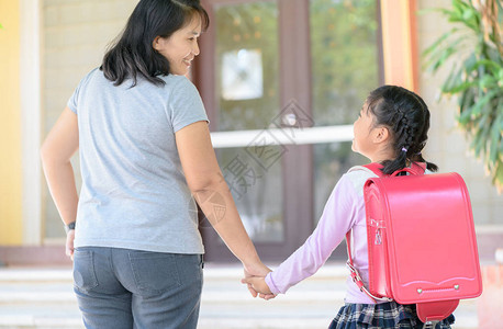 年轻母亲握着带背包女儿去上学的女儿的手图片