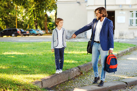 父子携手上学上课的开始秋天的第一天回到学校爸抱着他的孩子背包穿着西装的男人和男生一起散步时尚背景图片