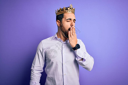 长着胡子的帅小伙戴着国王的金冠穿着紫色背景无聊趣的打哈欠手拉住嘴唇图片