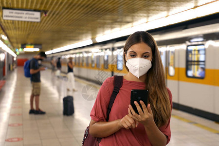 在地铁火车站使用智能电话应用程序对戴保护面罩的年轻图片
