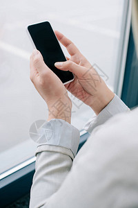 商业妇女使用智能手机在办公室窗口附近用空白屏幕显示的商业妇图片
