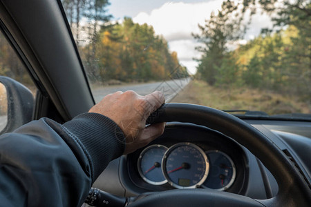 汽车的仪表板和方向盘的视图透过挡风玻璃可以看到道路和秋天的森林车速表转速表燃油表和冷却液温度指示器蓝色背景背景图片