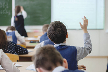 小学生举起手女孩少年女学生上课时在教室的黑板上写字教育培训儿童保育后视图背景图片