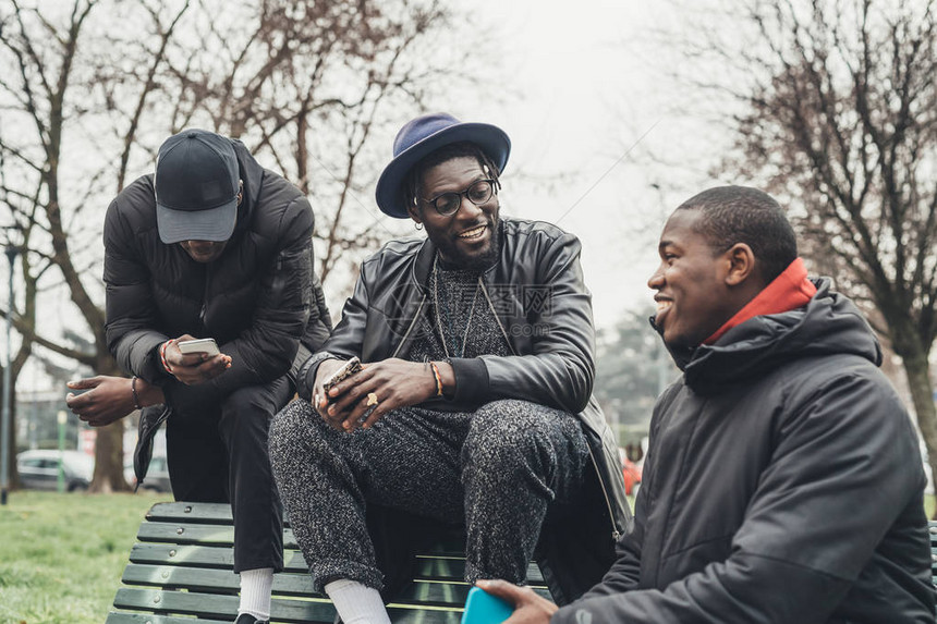 三个非洲朋友坐在户外看智能手机技术图片