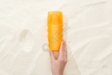 在金沙上涂橙色遮阳油膏的妇图片