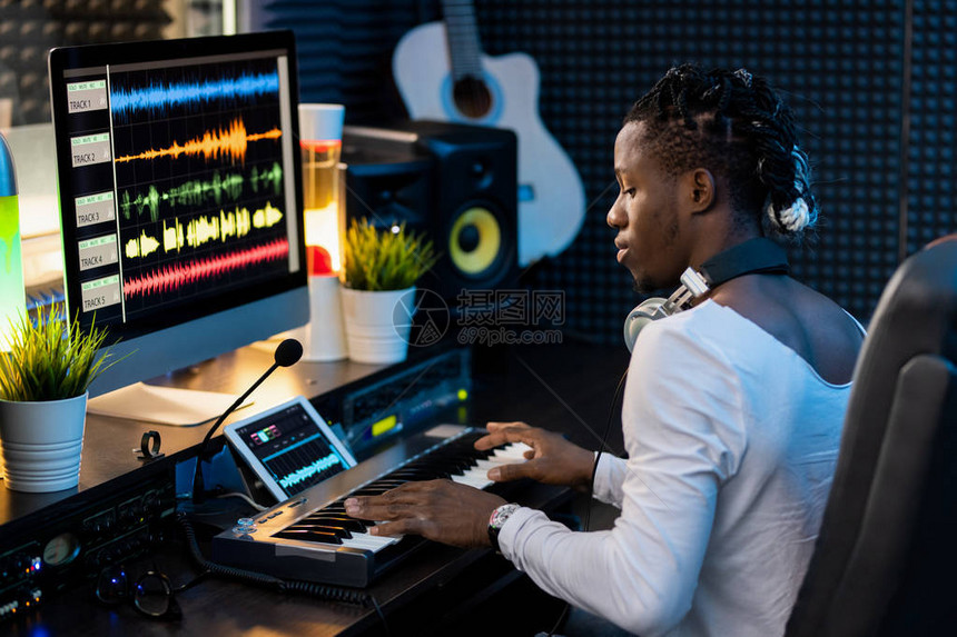 严肃的非洲青年男子按键钢琴键盘和用波形声音可视化看平板显图片