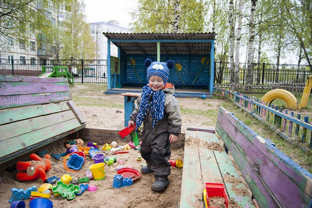 一个三岁的小男孩在一个凉爽的春日阳光明媚的日子里在幼儿园的沙箱里玩耍背景图片
