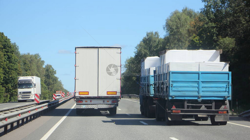 带白色货车拖的半卡车在郊区高速公路上超越装载的平板卡车图片