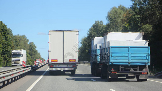 带白色货车拖的半卡车在郊区高速公路上超越装载的平板卡车背景图片