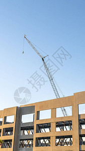 垂直的蓝天在由金属棒支撑的未完工建筑的框架上一台建筑起重机耸立在图片