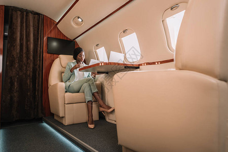 有自信的非洲女商人在私人飞机上喝咖啡和阅读报背景图片