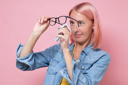 白种女人在粉红色的墙上用超细纤维纸巾清洁眼镜或片医疗保健视图片