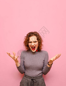 一个穿着时尚休闲服卷发在粉红色背景上的情绪化女孩的肖像图片