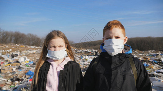 戴着医用防护面具的严肃男孩和女孩的肖像站在肮脏的垃圾场背景下图片