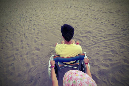 夏天沙滩轮椅上穿黄色T恤的小男孩在沙滩上背景图片