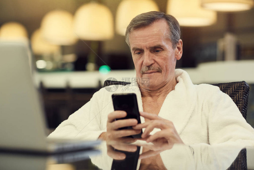 当代身穿浴袍高年长男子的肖像使用智能手机图片