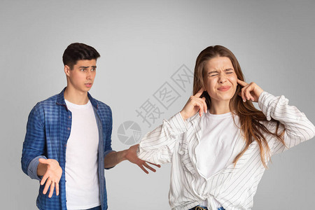 年轻夫妇吵架女孩用手捂住耳朵灰色背景图片