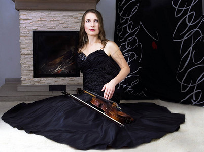 身着黑裙子的小提琴手坐在壁炉附近背景图片