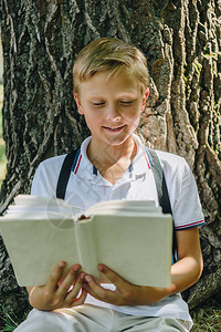 可爱的微笑小学生坐在树旁看书图片