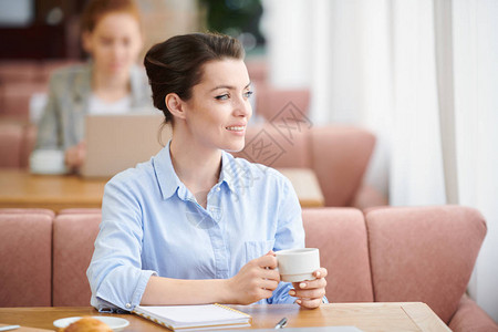 穿着蓝上衣坐在桌边喝咖啡下班后在咖啡馆休息的年轻女商人图片