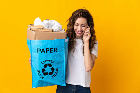 年轻女人拿着一个回收袋满纸的废纸来回收在黄色背景笑声中图片