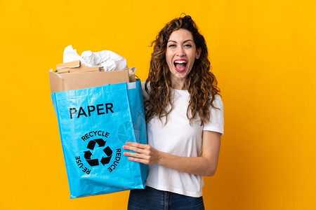 年轻女拿着一个回收袋满纸的张来回收在黄色背景上孤立的循环用图片