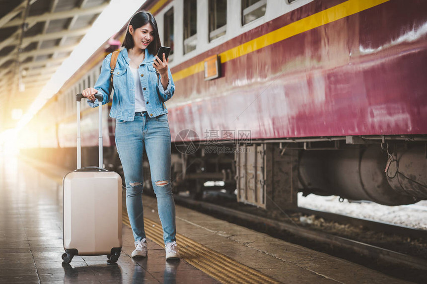 在火车站平台使用智能手机携带行李旅行背包行李的亚洲妇女快图片