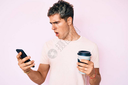 年轻英俊的男人拿着智能手机拿着震惊的脸拿走咖啡图片