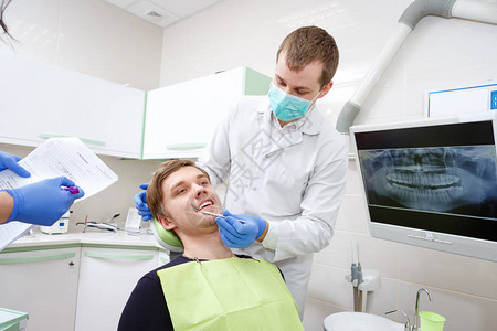 向牙科诊所的年轻牙医男显示牙齿图片