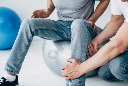 在医院里坐在健身球上的病人的生理治疗师按摩腿图片