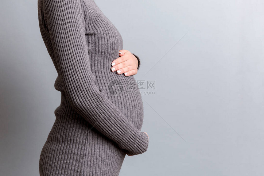 身着灰色裙子的孕妇紧抱住她的腹部在灰色背景母概图片