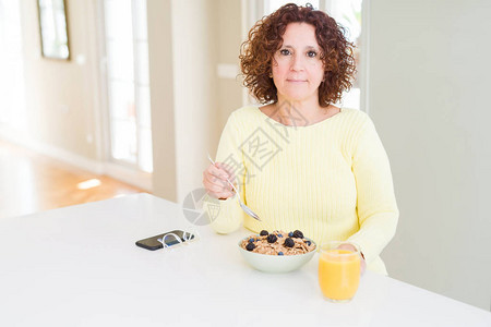 早晚在家吃健康早餐的年长女人在聪明的面孔上自信地表情图片