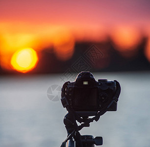 三脚架上的数字摄影机拍摄湖边日落的照片图片