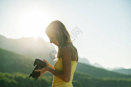 年轻女摄影师站在天亮的外边检查摄像背景图片