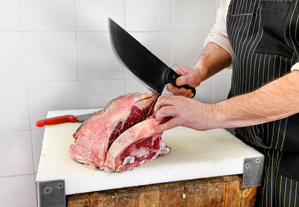屠夫用大刀割牛排在屠宰场的屠宰板上切肋目牛图片